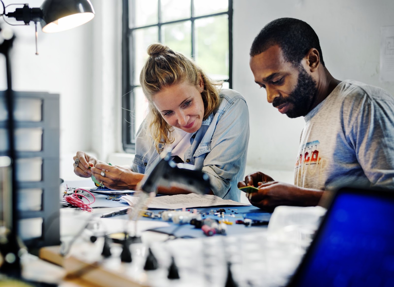 Engineers smiling and working on electronic components at a workbench.