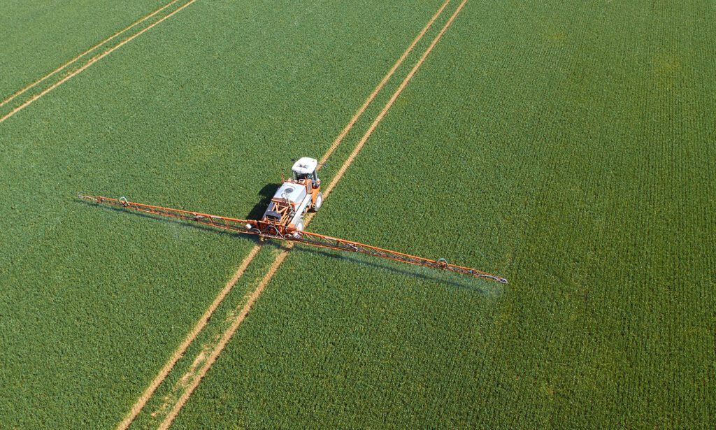 A white and orange crop sprayer, seen in a field from an aerial view.
