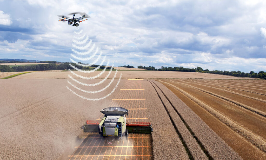 A futuristic drone robot sending communications down to an agricultural robot in a wheat field.
